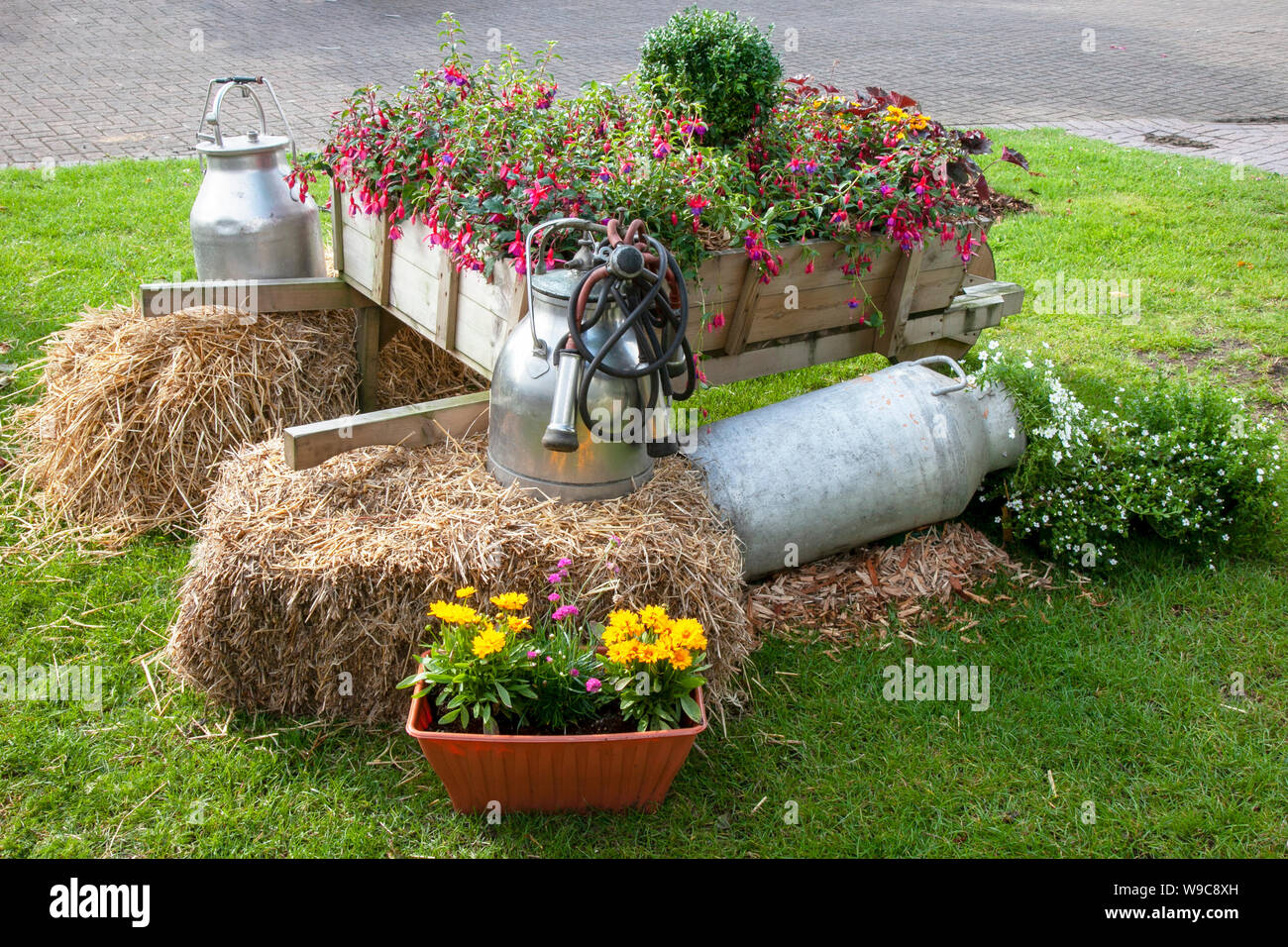 A rustic old wooden wheelbarrow filled with colorful flowers, Dairy milking farm equipment, milk churns, straw bales, at Southport Flower Show, Victoria Park, UK Stock Photo