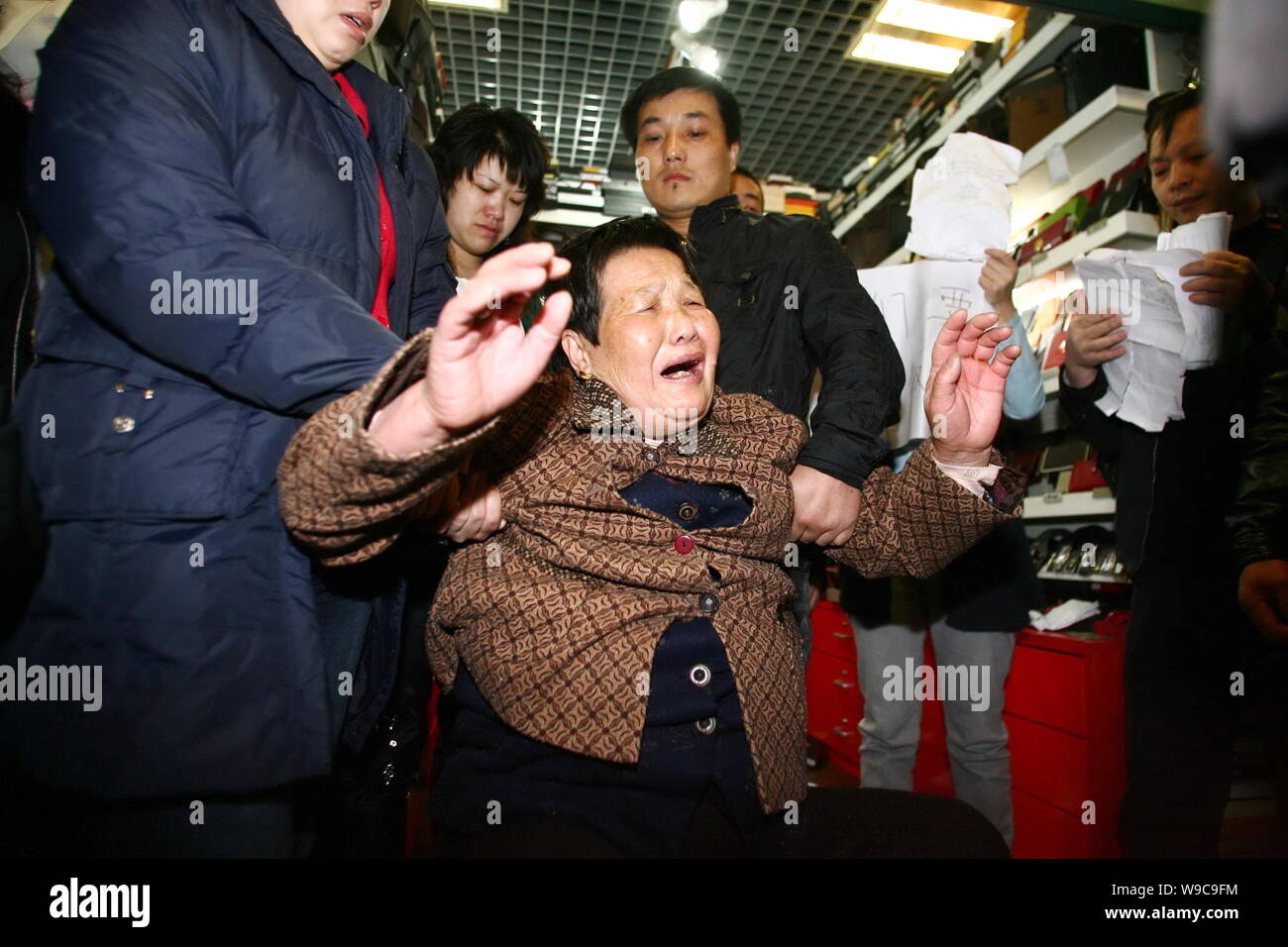 A Chinese elderly woman, middle, the mother of a Chinese stall owner who is suspected of selling fake goods, reacts while security guards and administ Stock Photo