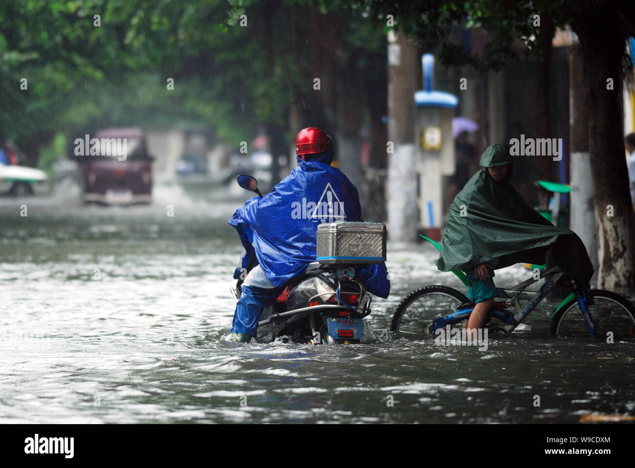 Chinese cyclists rides their bikes through a flooded street after heavy rain caused by Tropical Storm Parma in Haikou city, south Chinas Hainan provin Stock Photo