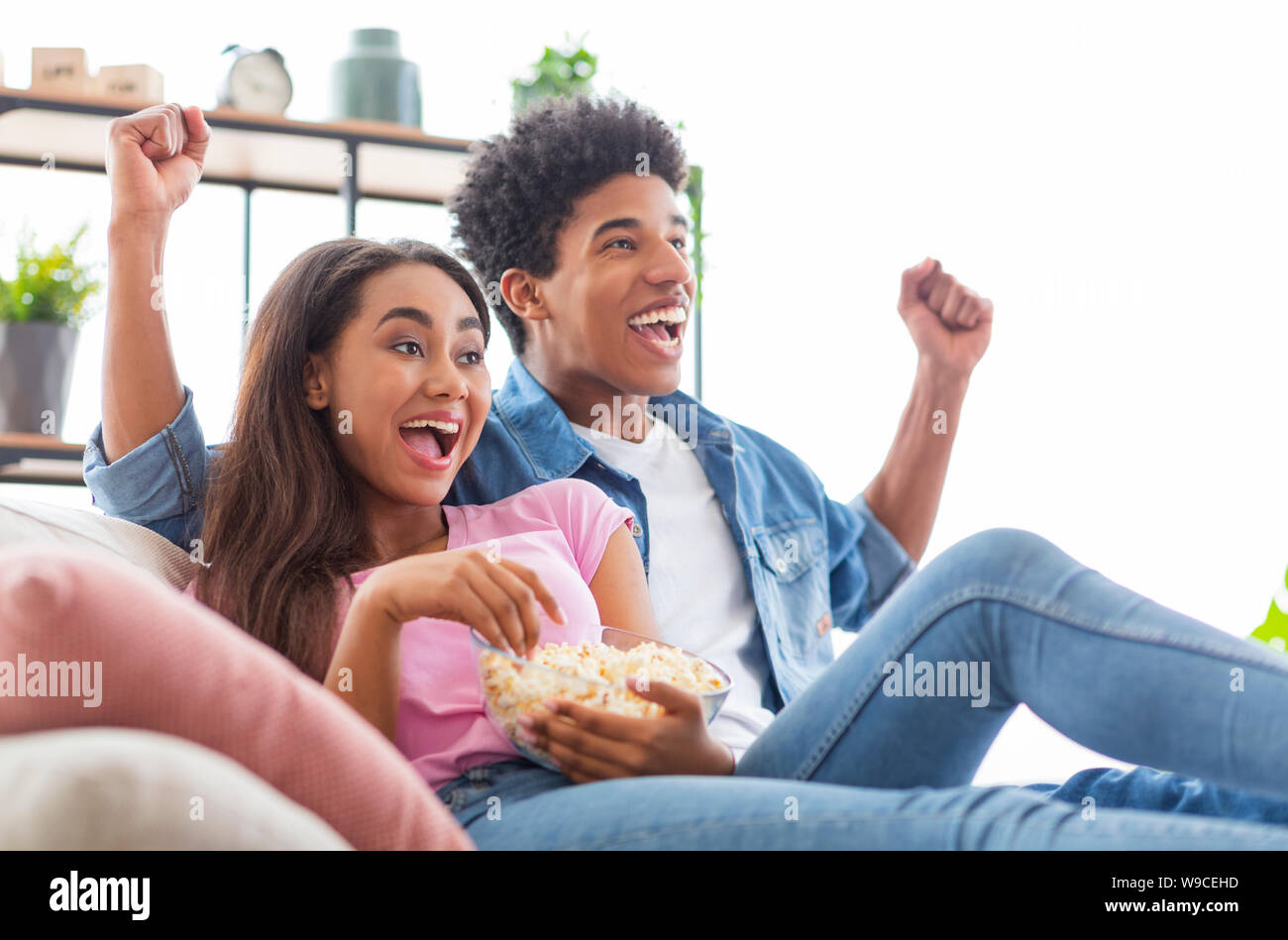 Black teen couple watching tv, sitting with popcorn at home Stock Photo ...