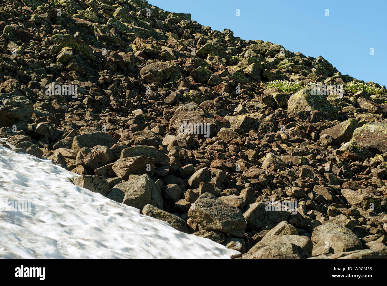 fragment of a stone scree on a slope on the edge of a melting glacier and a blue summer sky Stock Photo