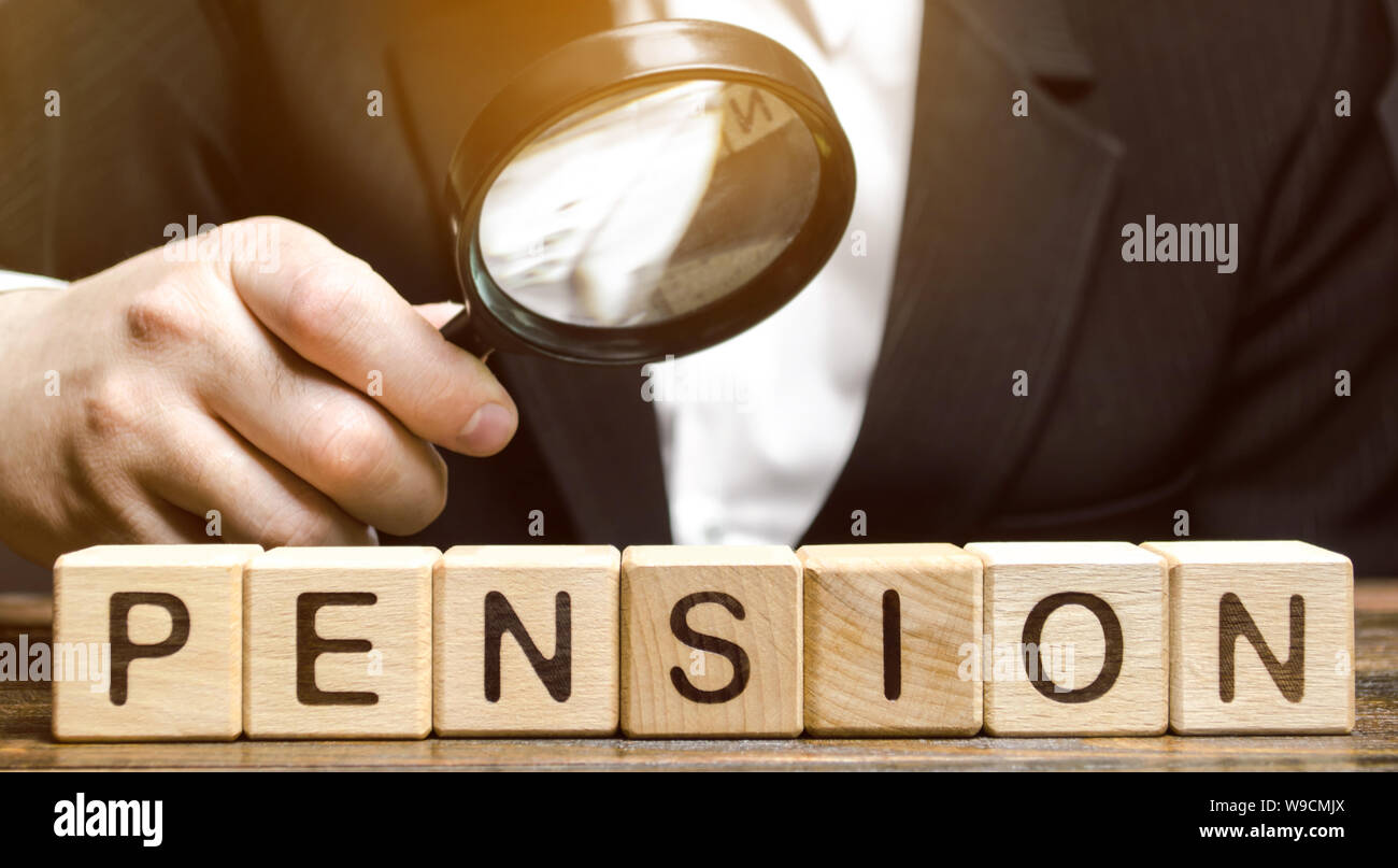 Wooden blocks with the word Pension and a magnifying glass in the hand of a man. Analysis of retirement payments. The size of pensions. Pension Fund. Stock Photo