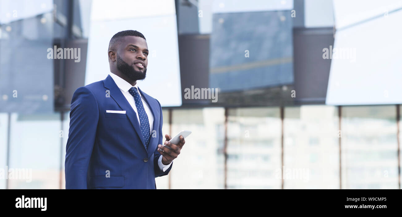 Pensive Black Business Man Holding Smartphone Standing In Urban Area Stock Photo