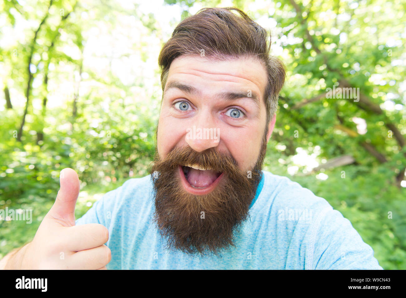 Thumbs up for bearded and beardy. Bearded man giving thumbs up hand gesture  on natural landscape. Bearded hipster gesturing on summer day. Brutal guy  wearing mustache and beard on bearded face Stock