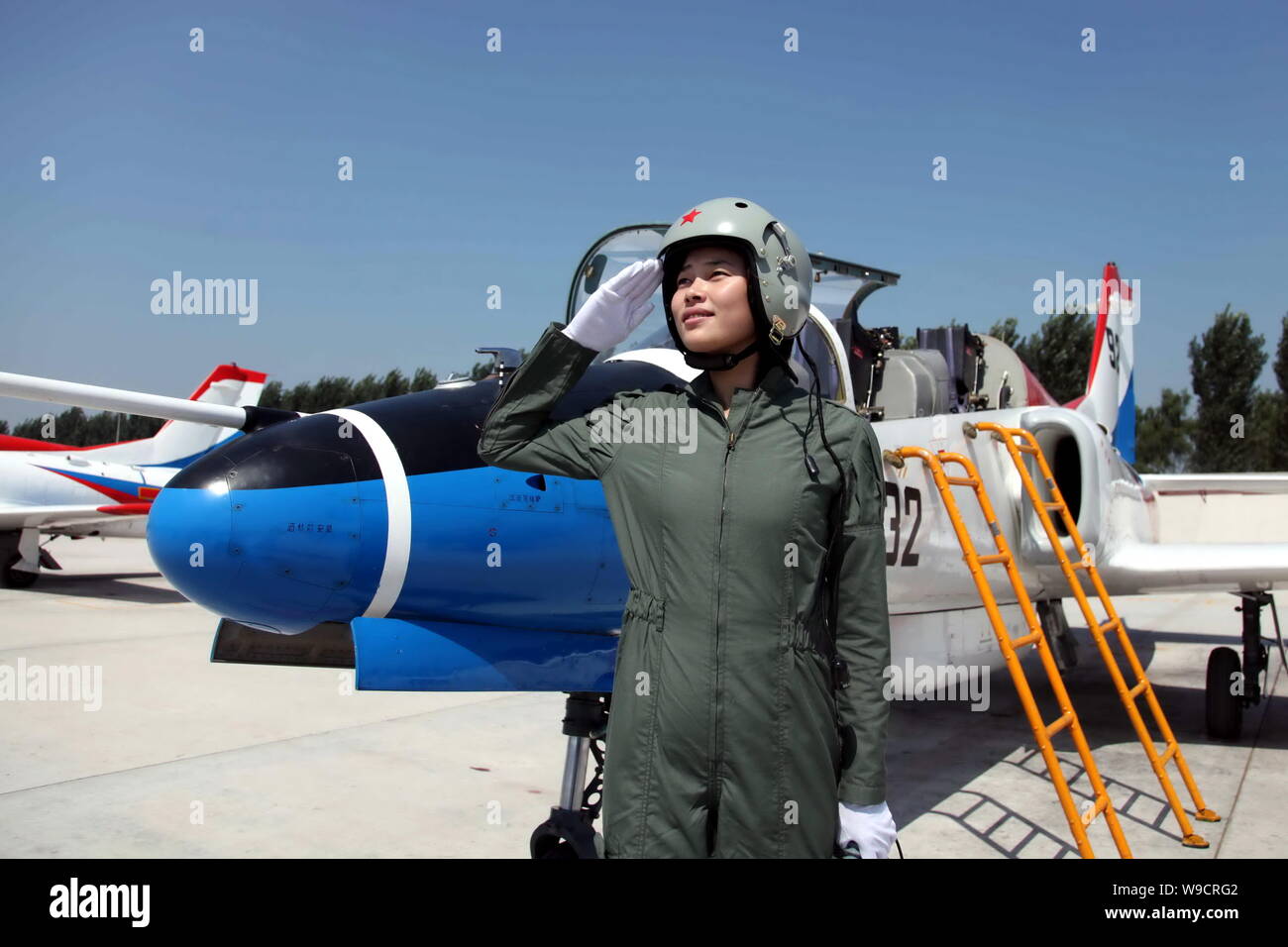 A young female fighter plane pilot of Chinese PLA Air Force salutes next to a training plane after a new flight suits delivery ceremony at an airport Stock Photo