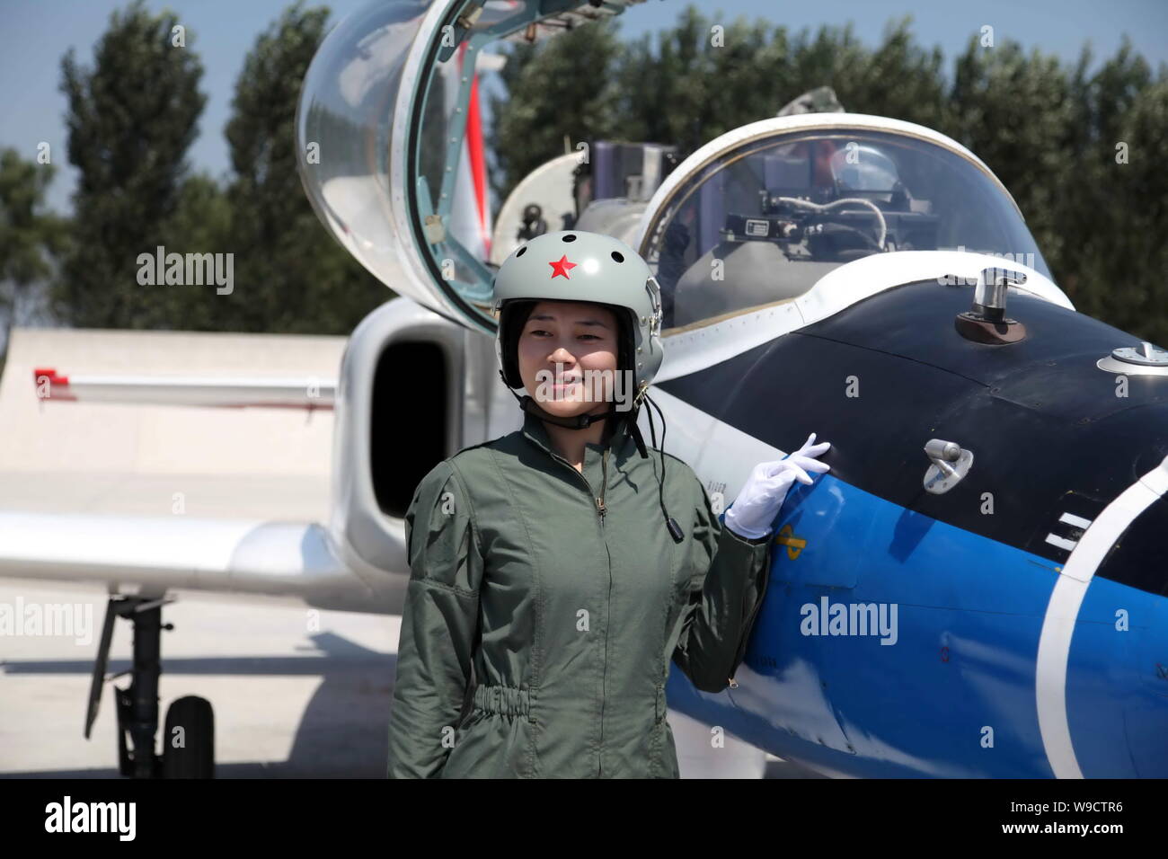 A young female fighter plane pilot of Chinese PLA Air Force poses next to a training plane after a new flight suits delivery ceremony at an airport in Stock Photo