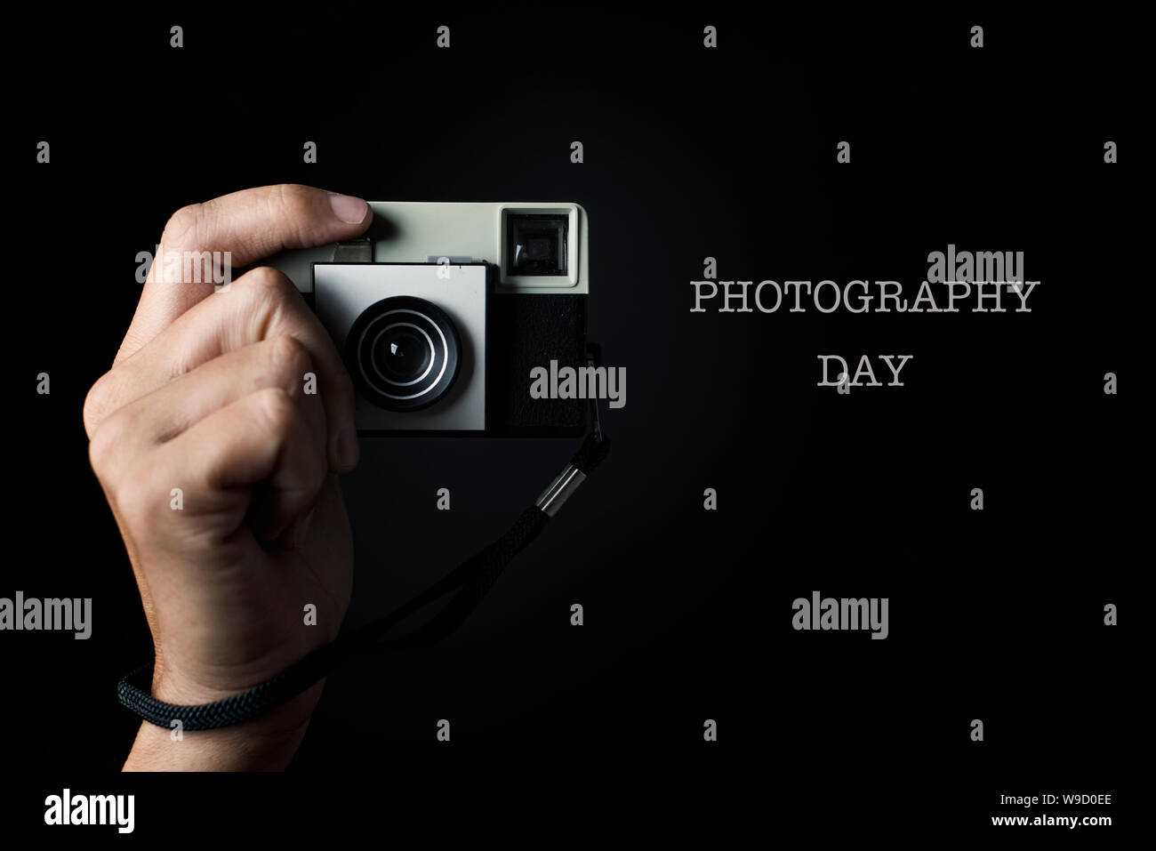 the hand of a man about to press the shutter button of a retro film camera, pointing to the observer, and the text photography day Stock Photo