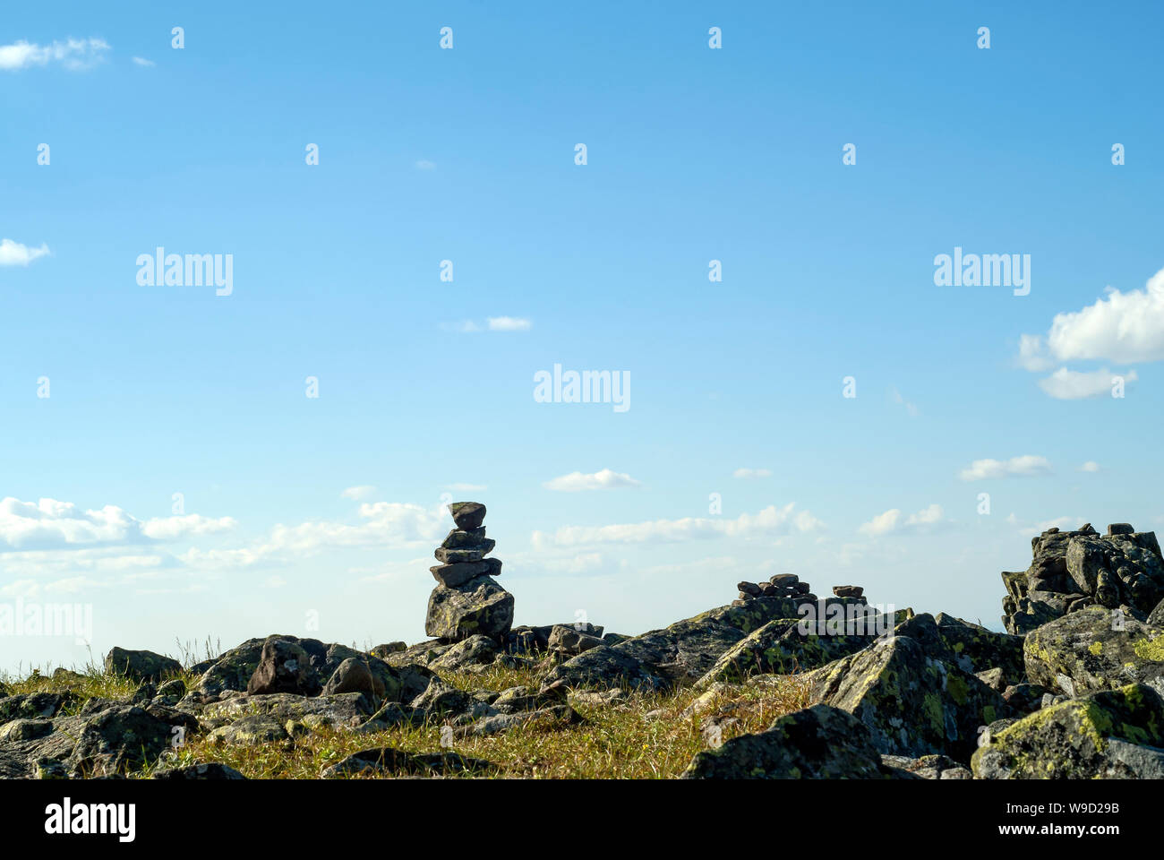 bright landscape of a high-altitude plateau with folded travelers pyramid cairn of stones under a blue sky with clouds Stock Photo
