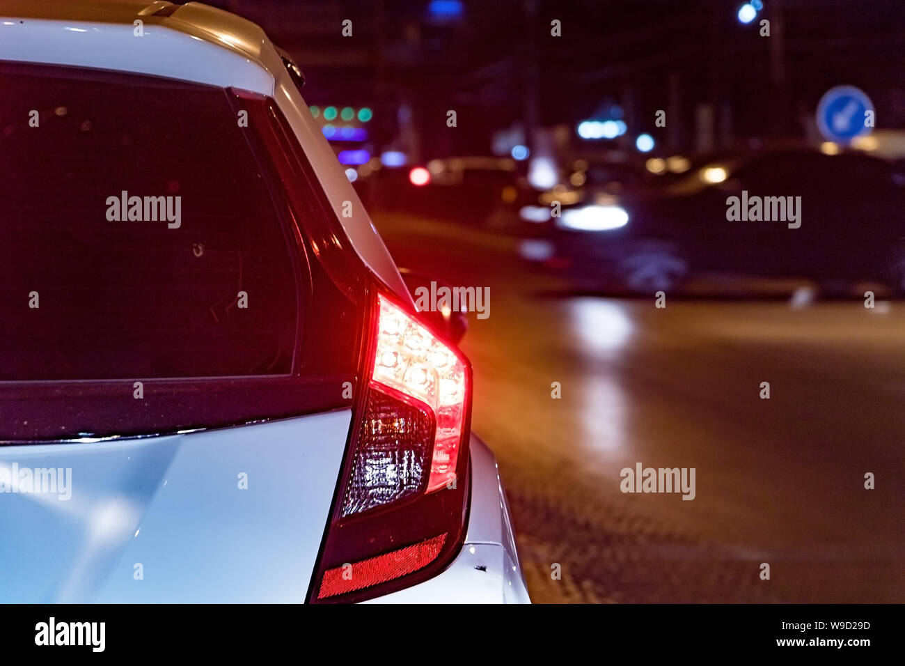A tail-light of car at night city. A red light at the rear of a white car waiting at crossroad. Stock Photo