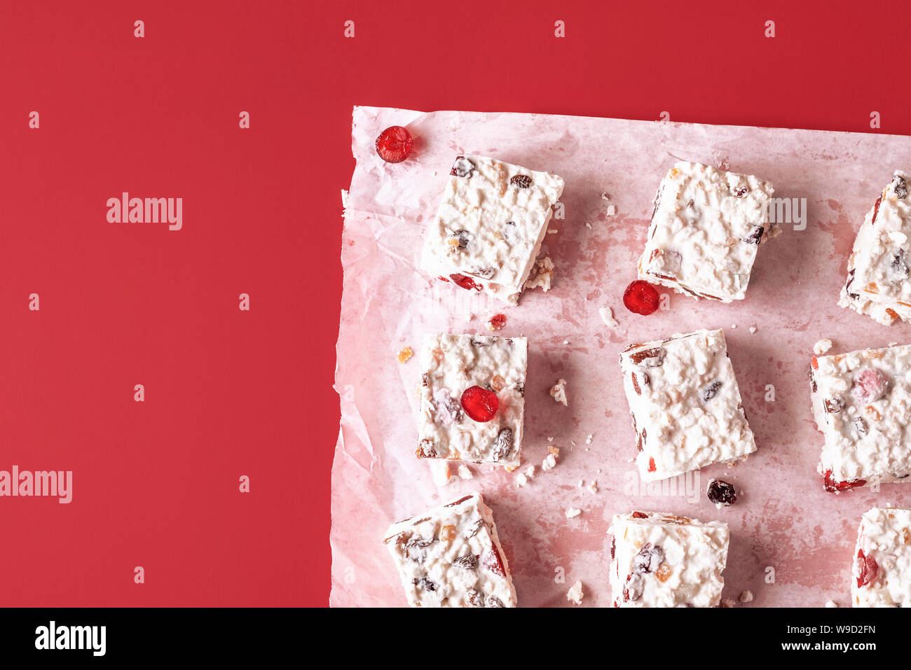 Australian Christmas dessert with dried fruits and coconut, cut in pieces, on red background. Flat lay of white cake with rice. Traditional Xmas food Stock Photo