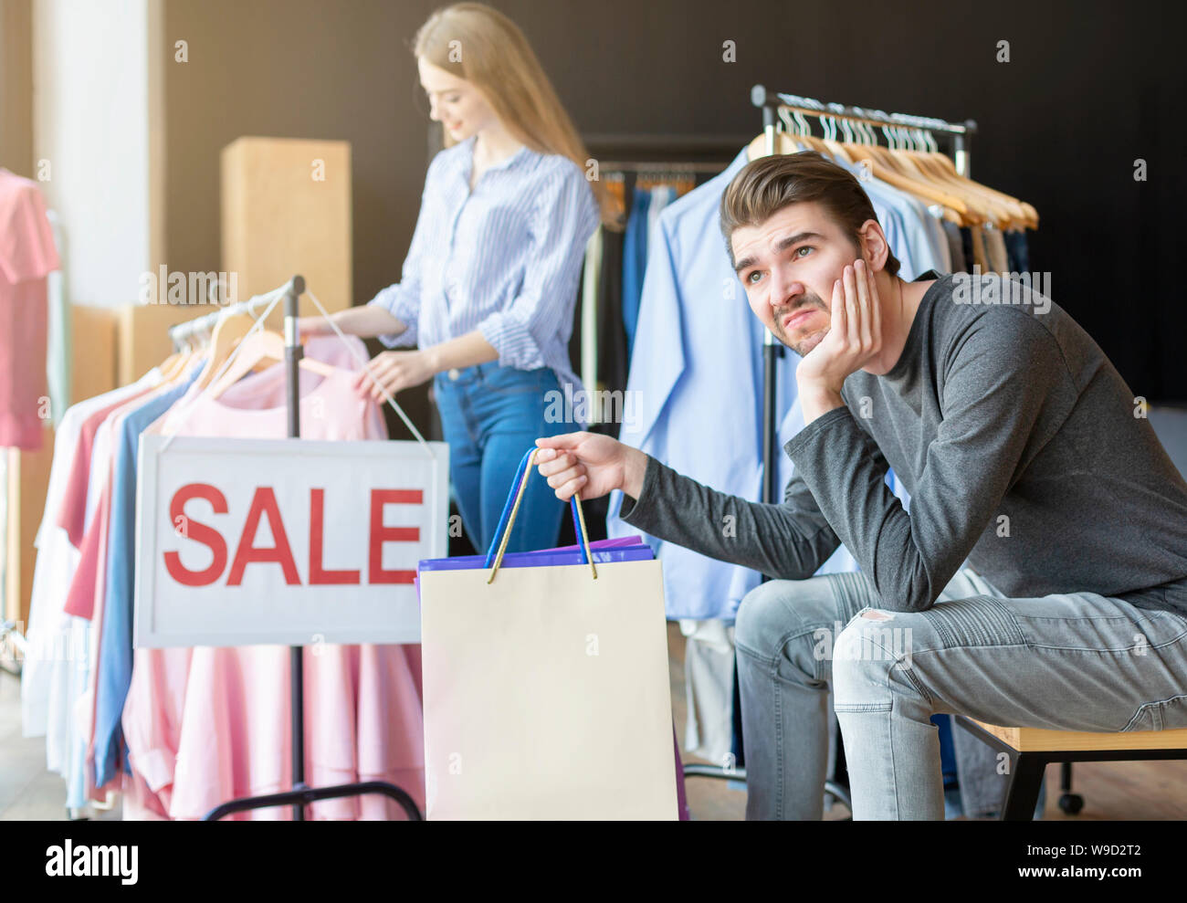 Bored boyfriend waiting while his girlfriend choosing clothes Stock Photo