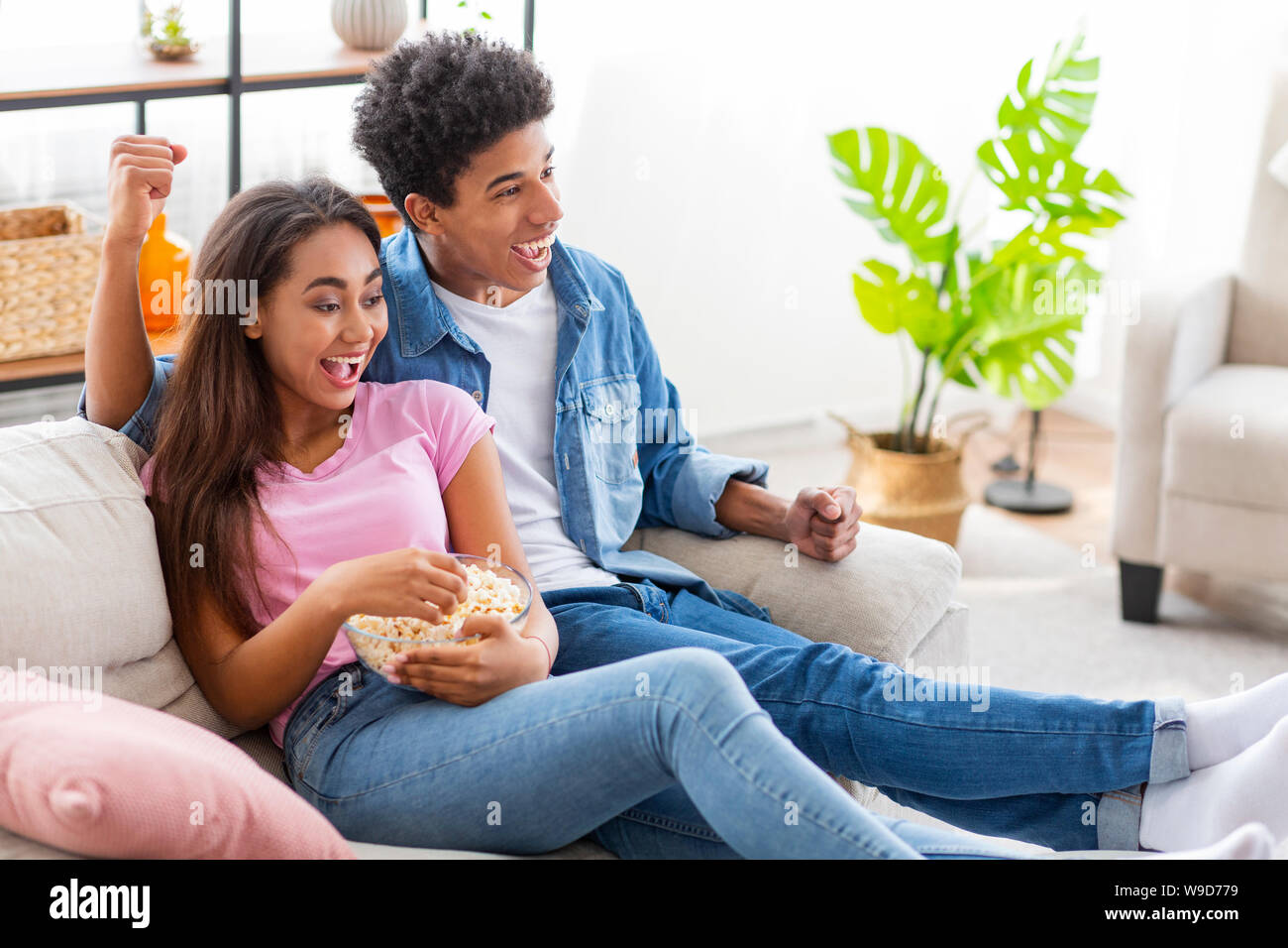 African Couple Watching Sports On Television And Cheering Stock Photo