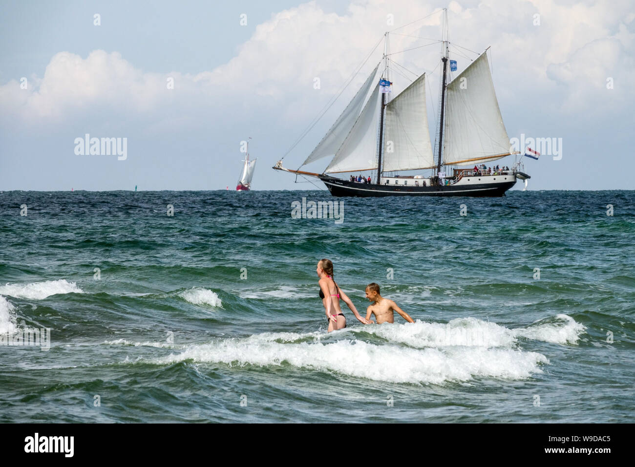 Rostock Germany, two teenagers bathing in the baltic sea enjoying the romp in the waves at the beach in Warnemunde, Sailboats sail by sea Stock Photo