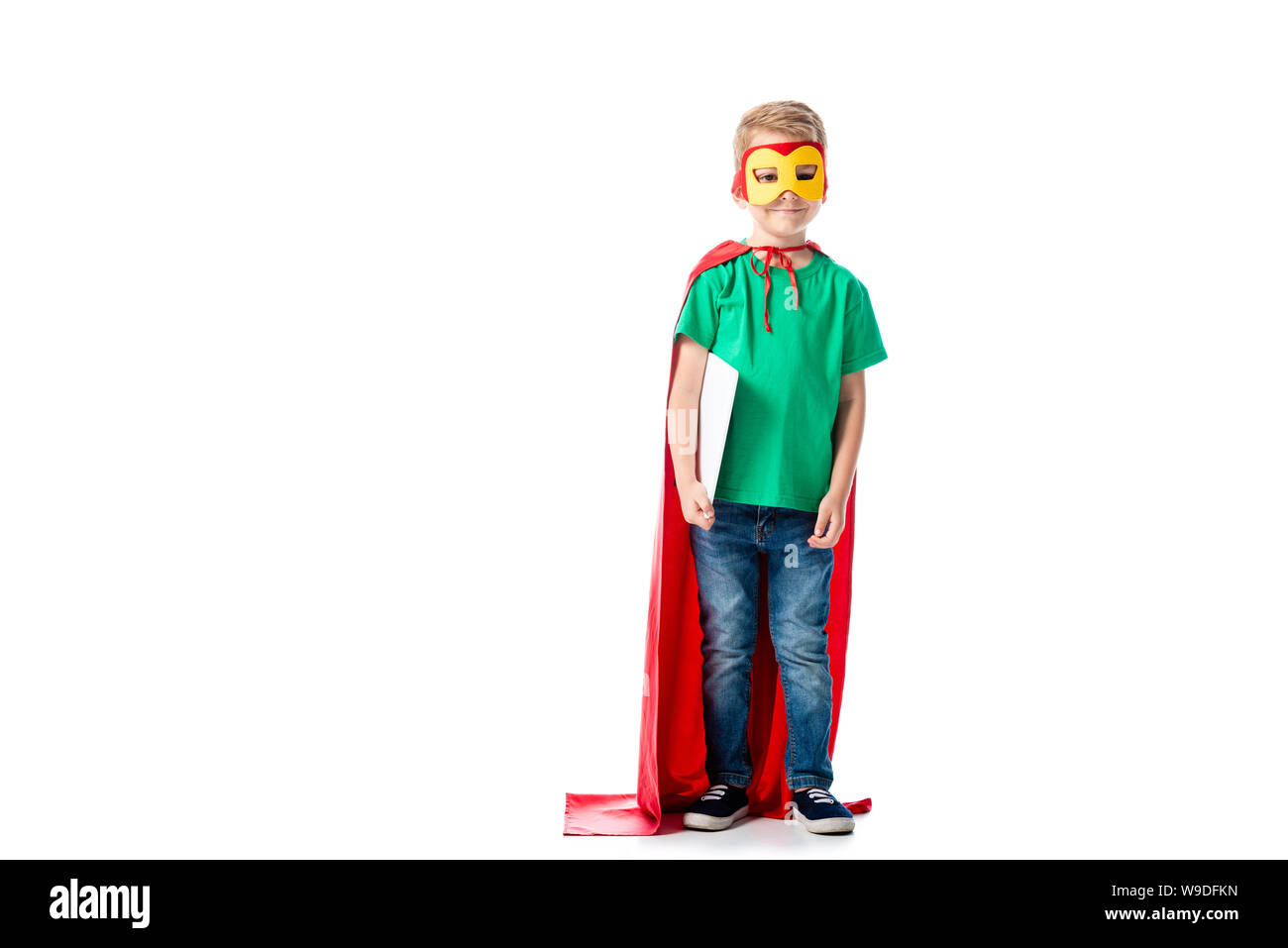 full length view of preschooler kid in mask and hero cloak holding digital tablet on white Stock Photo
