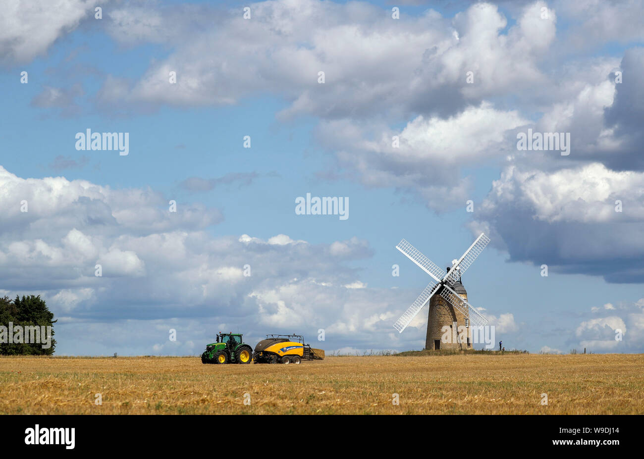 A bailer works in a field in front of Great Haseley windmill in Oxfordshire. Stock Photo