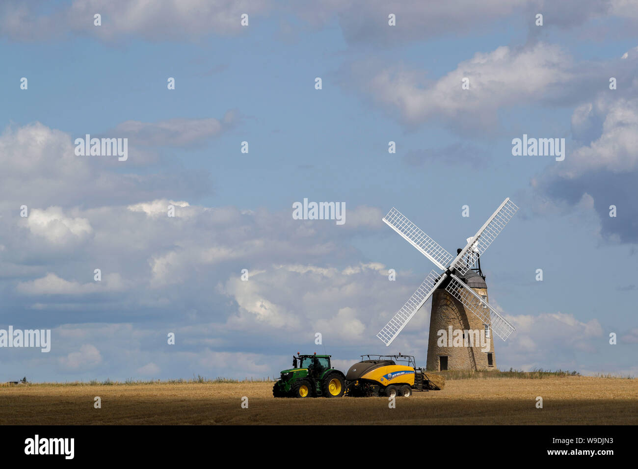A bailer works in a field in front of Great Haseley windmill in Oxfordshire. Stock Photo