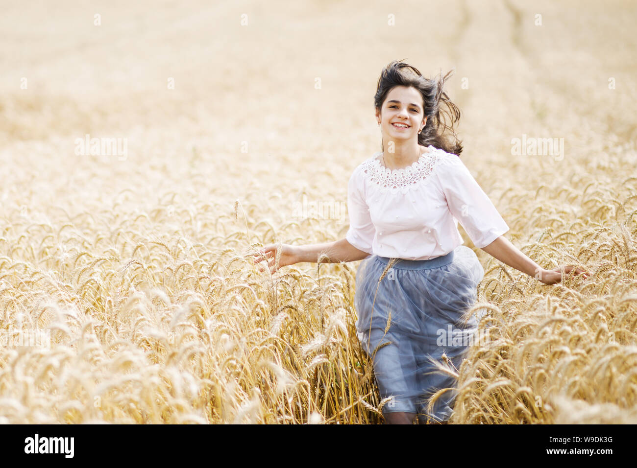 Beauty Girl Outdoors enjoying nature. Beautiful Teenage Model girl running on wheat field Stock Photo