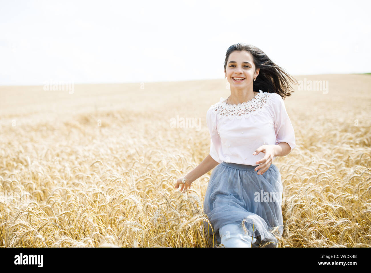 Beauty Girl Outdoors enjoying nature. Beautiful Teenage Model girl running on wheat field Stock Photo