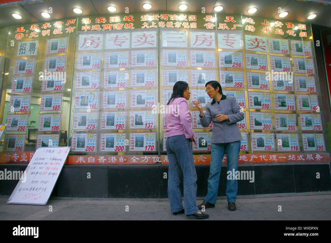 Chinese women talk in front of advertisements of second-hand houses outside a real estate agency in Shanghai, China, 4 November 2008.   Property price Stock Photo
