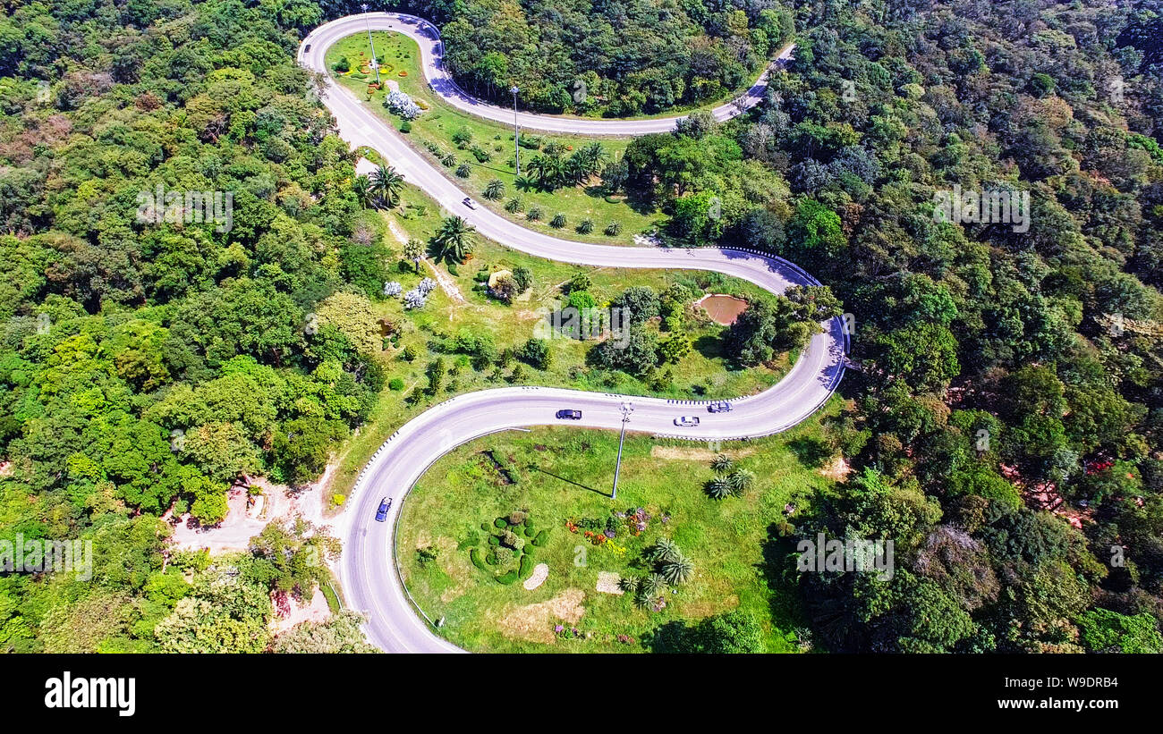 Aerial view from drone of cars are going through a curve road on the mountain with green forest. The transportation road across mountain. Stock Photo