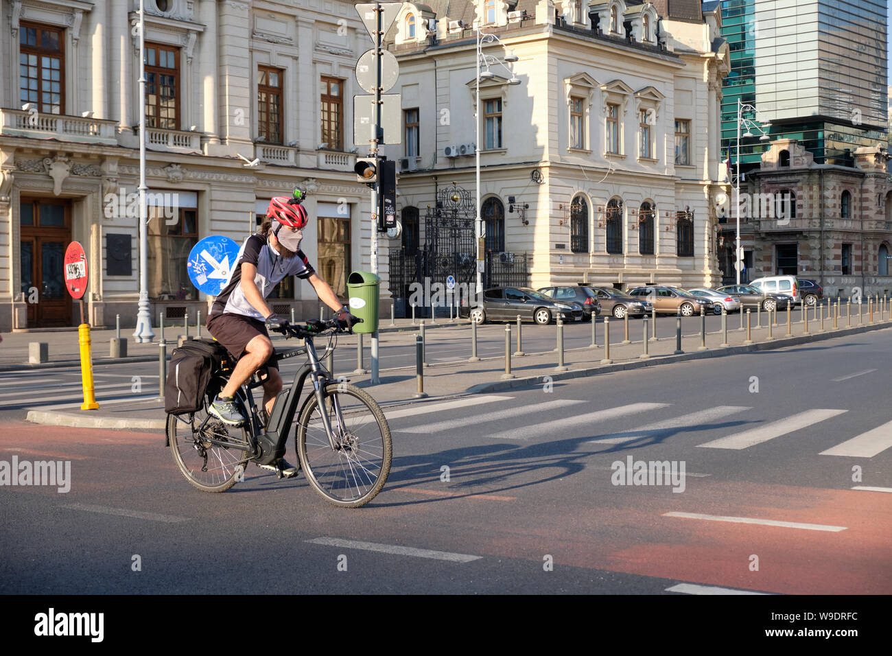 Cyclist with Helmet, camera and top, pollution mask crosses street on cycling lane in downtown Bucharest, Romania, Stock Photo