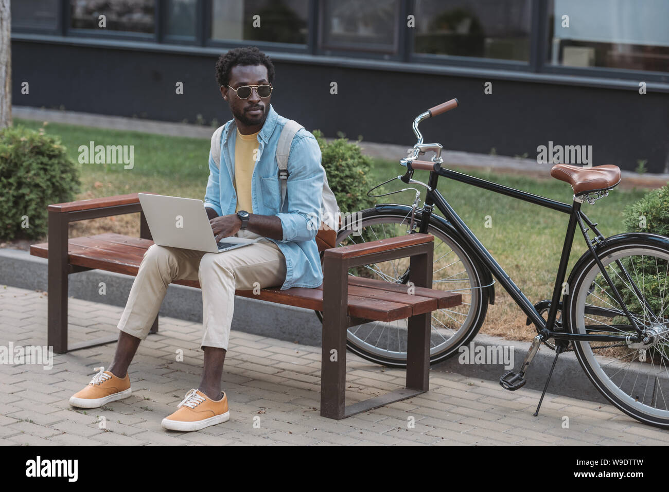 handsome african american man using laptop while sitting on bench near ...