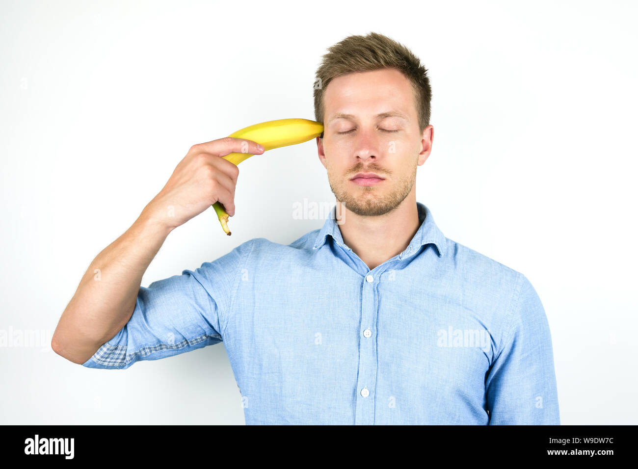 young handsome man holding banana as a gun at his temple on isolated