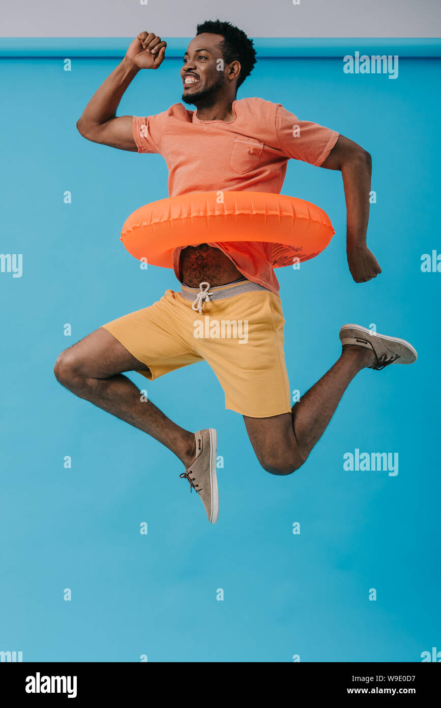 cheerful bearded african american man jumping with swim ring on blue Stock Photo