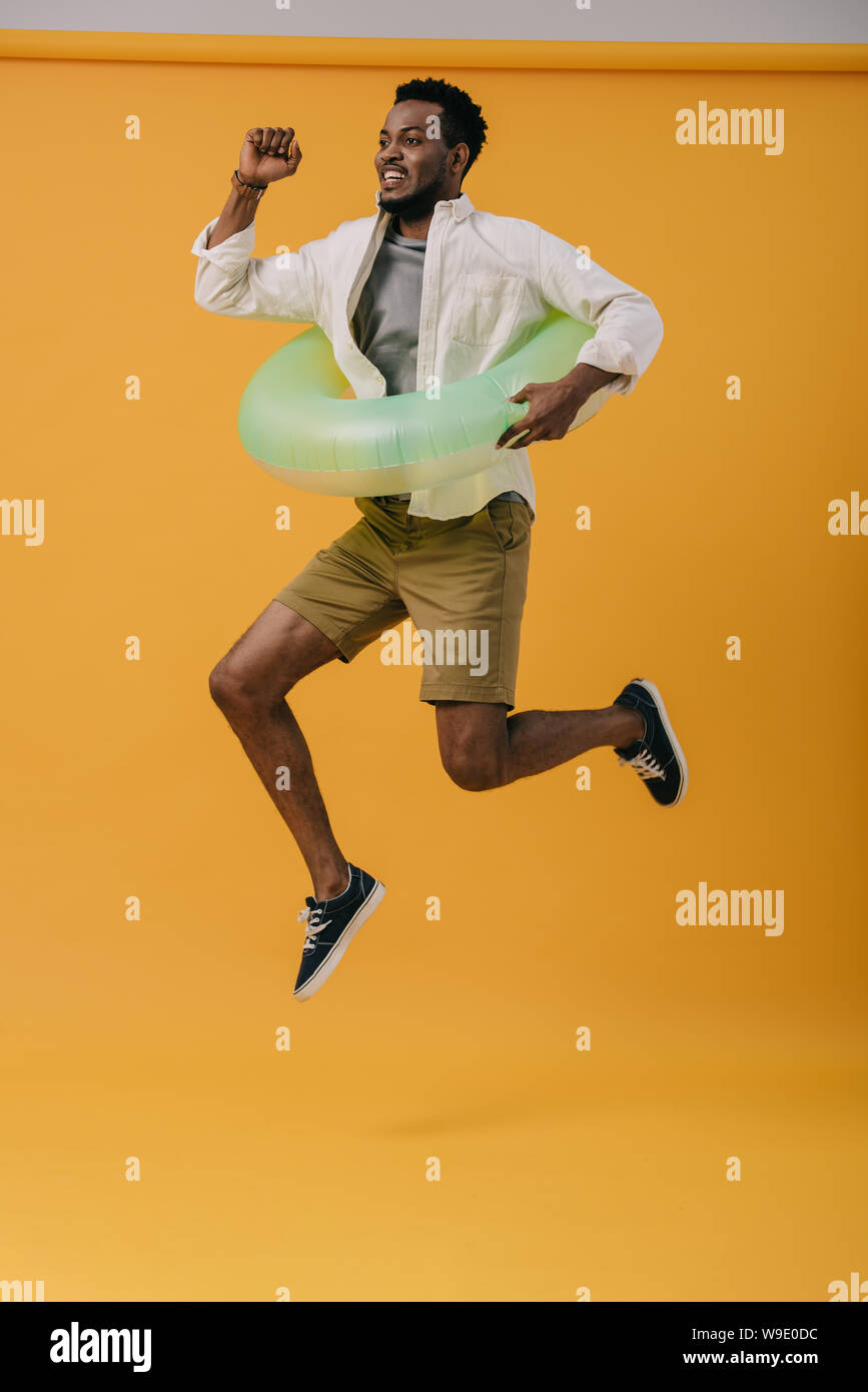 cheerful bearded african american man jumping with swim ring on orange Stock Photo