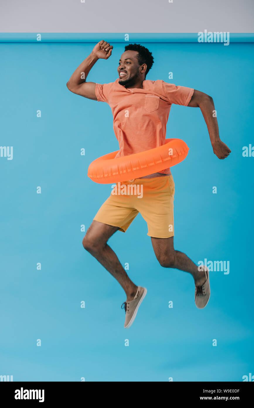 happy bearded african american man jumping with swim ring on blue Stock Photo