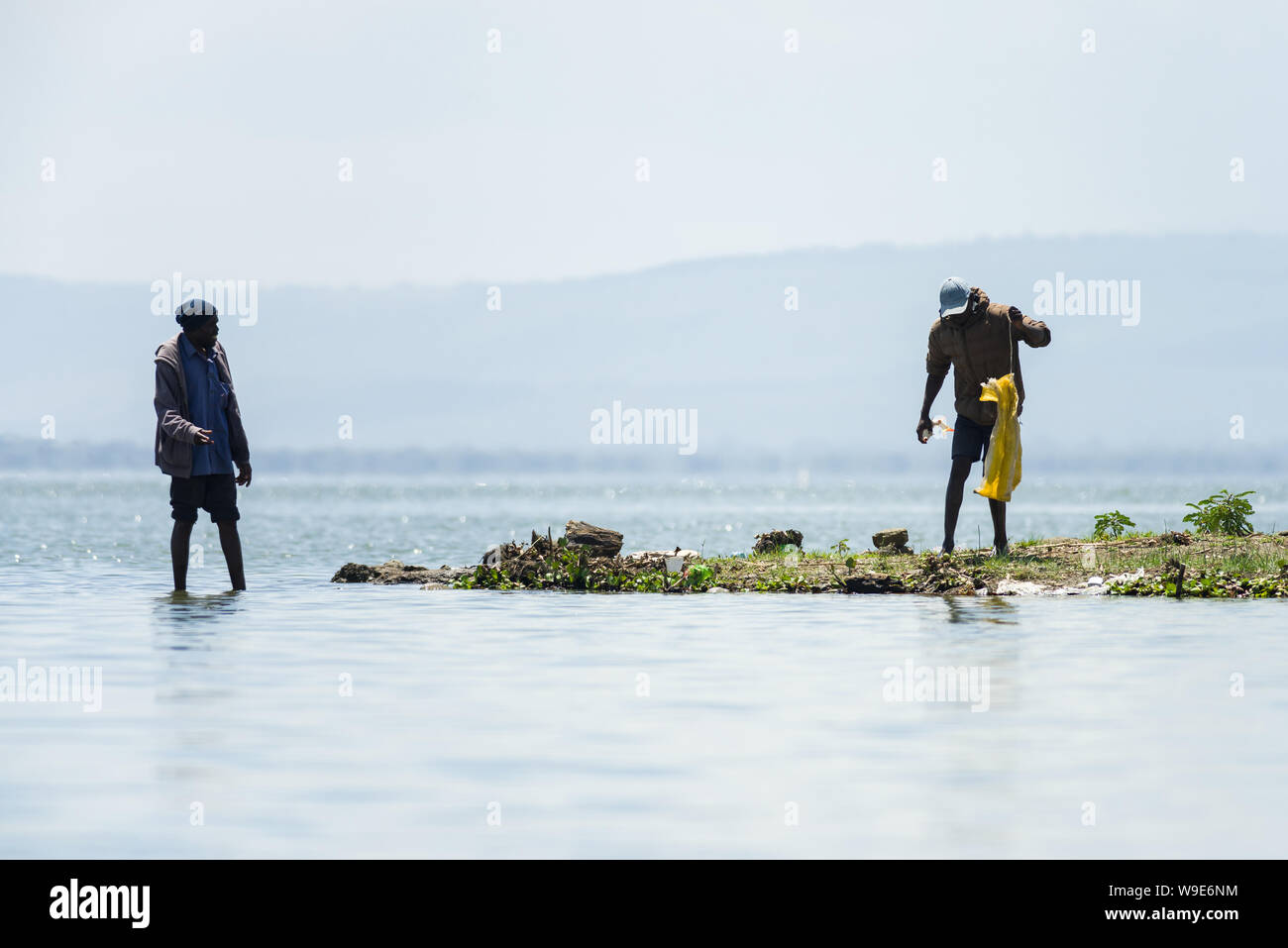 Two Kenyan fishermen stand by the shore catching fish, lake Naivasha, Kenya, East Africa Stock Photo