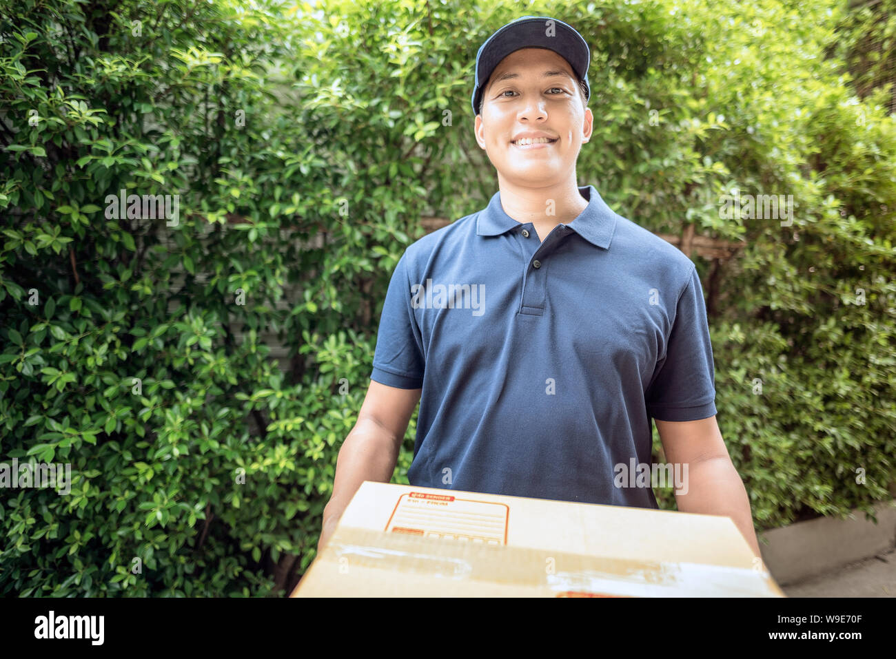 Asian delivery man smiling while holding a cardboard box delivery to his customer. Stock Photo