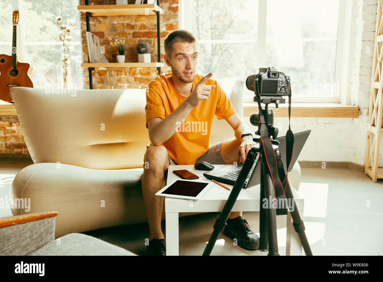 Young caucasian male blogger with professional camera recording video review of gadgets at home. Blogging, videoblog, vlogging. Man making vlog or live stream about photo or technical novelty. Stock Photo