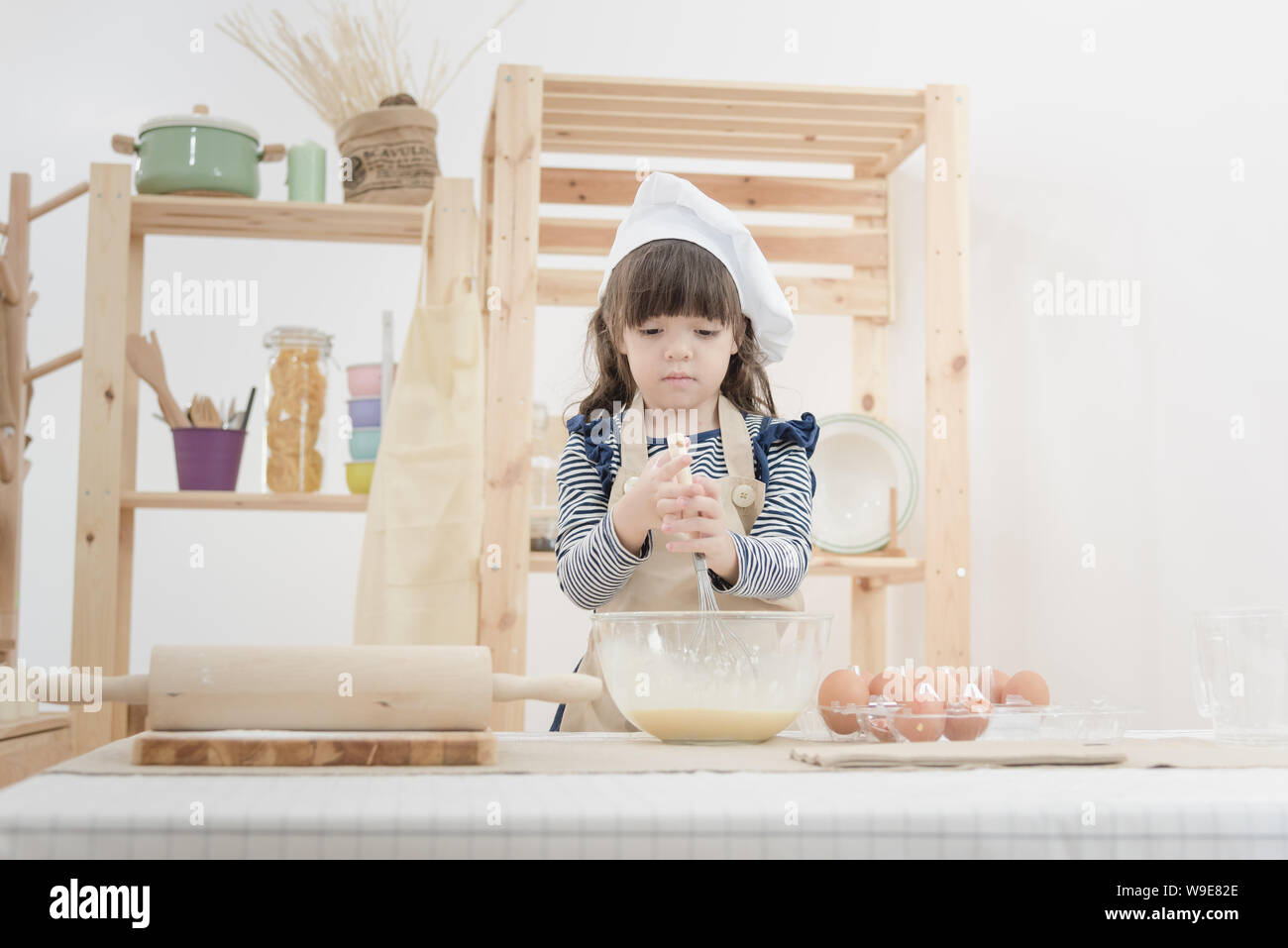 Cute kid enjoy preparing the dough to make a cake in the kitchen room.Photo series of Happy family concept. Stock Photo