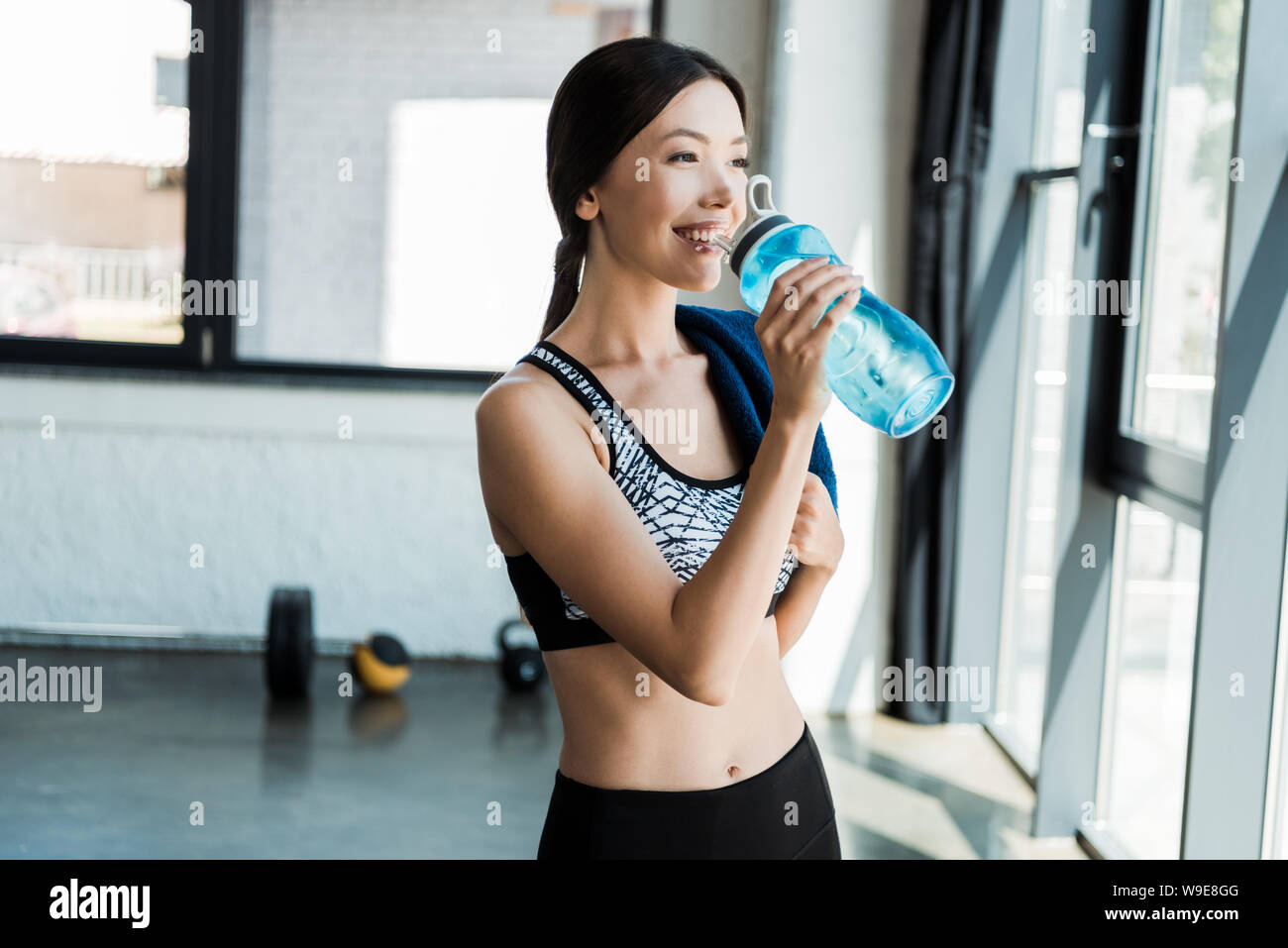https://c8.alamy.com/comp/W9E8GG/happy-girl-drinking-water-while-holding-sport-bottle-in-gym-W9E8GG.jpg