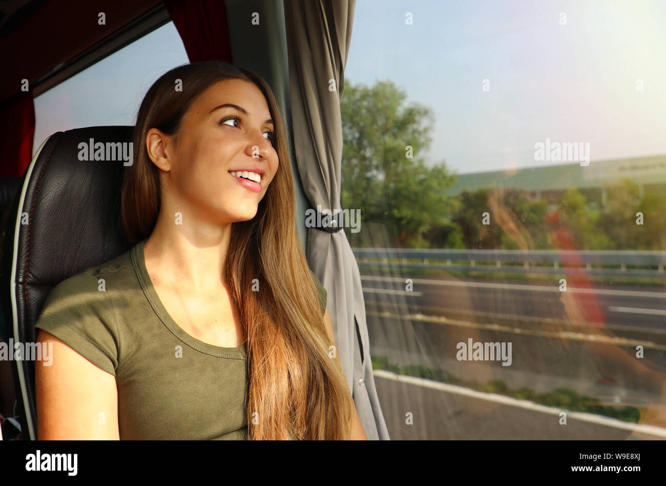 Young beautiful woman looking through the bus window. Happy bus passenger traveling sitting in a seat and looking through the window. Stock Photo