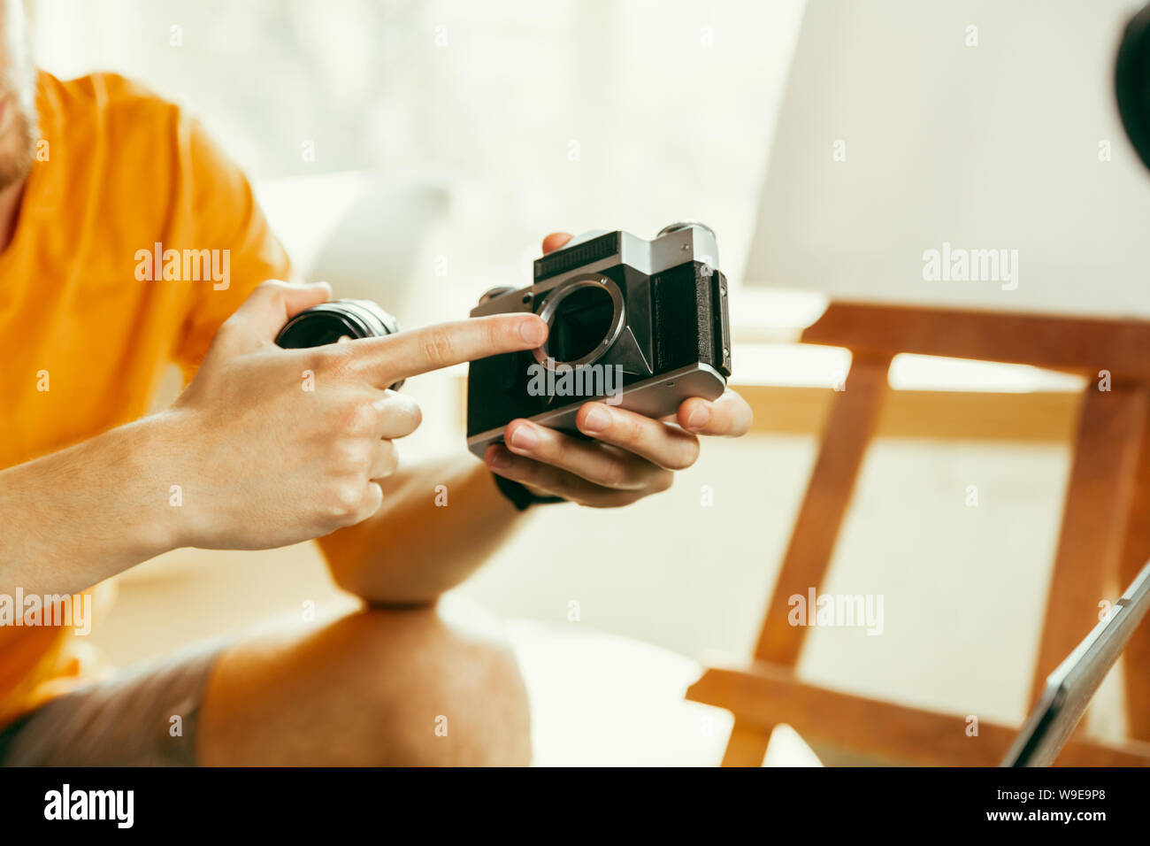 Young caucasian male blogger with professional equipment recording video review of camera at home. Blogging, videoblog, vlogging. Man making vlog or live stream about photo or technical novelty. Stock Photo