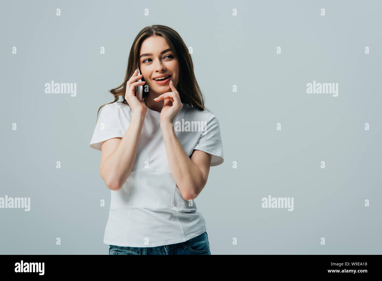 cunning beautiful girl in white t-shirt talking on smartphone isolated on grey Stock Photo