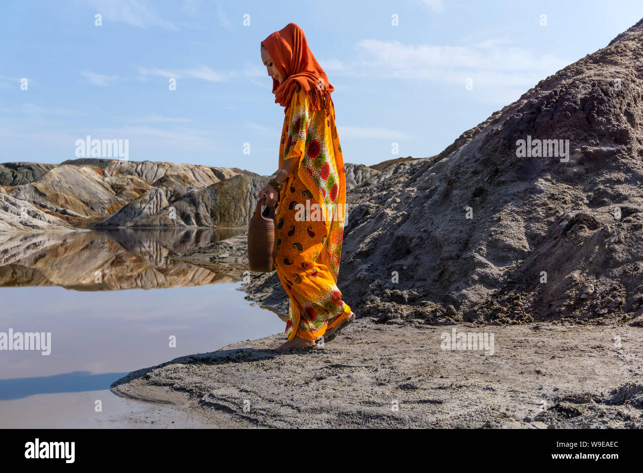 girl of oriental appearance in a sari and hijab with a jug by the lake in the desert Stock Photo