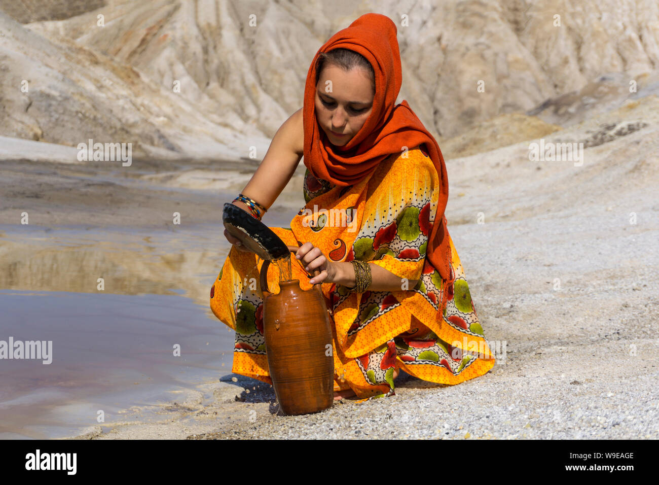 girl of oriental appearance in sari and hijab fills the pitcher with water from a dirty source in the arid area Stock Photo