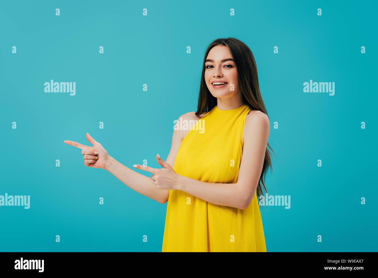 happy beautiful girl in yellow dress pointing with fingers aside ...
