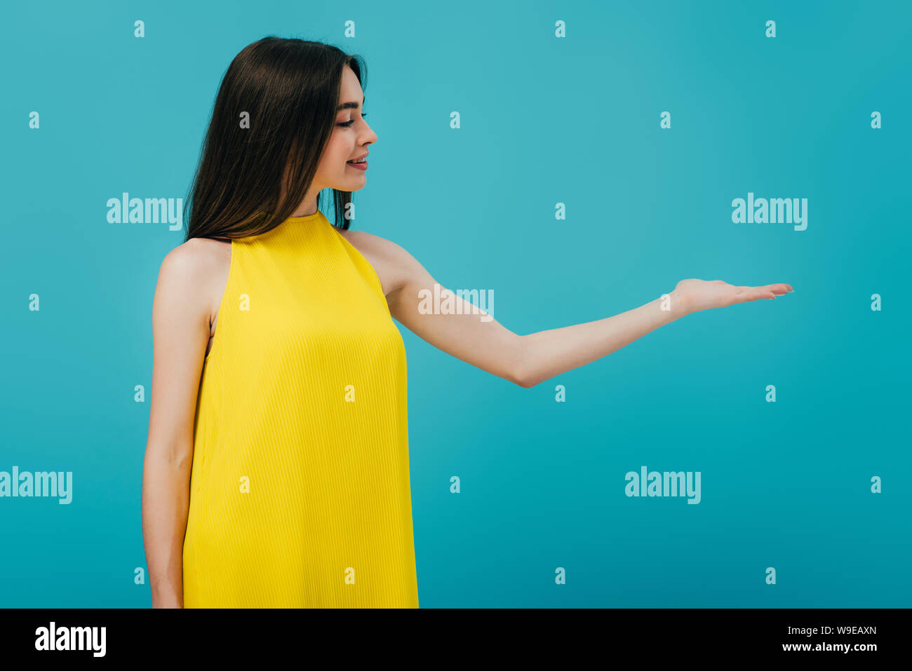 happy beautiful girl in yellow dress pointing with hand at copy space ...