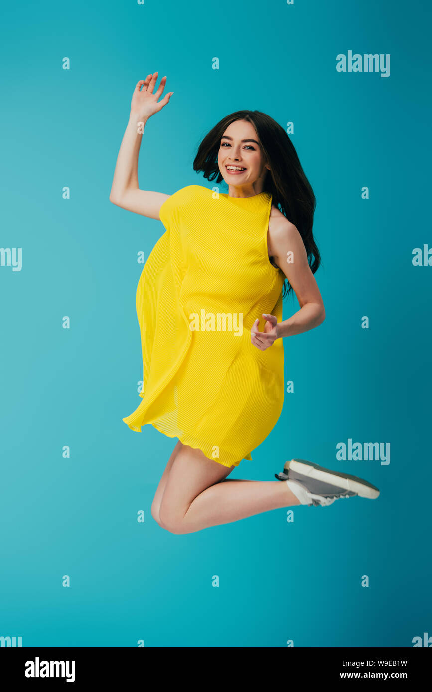 full length view of happy beautiful girl in yellow dress jumping on ...