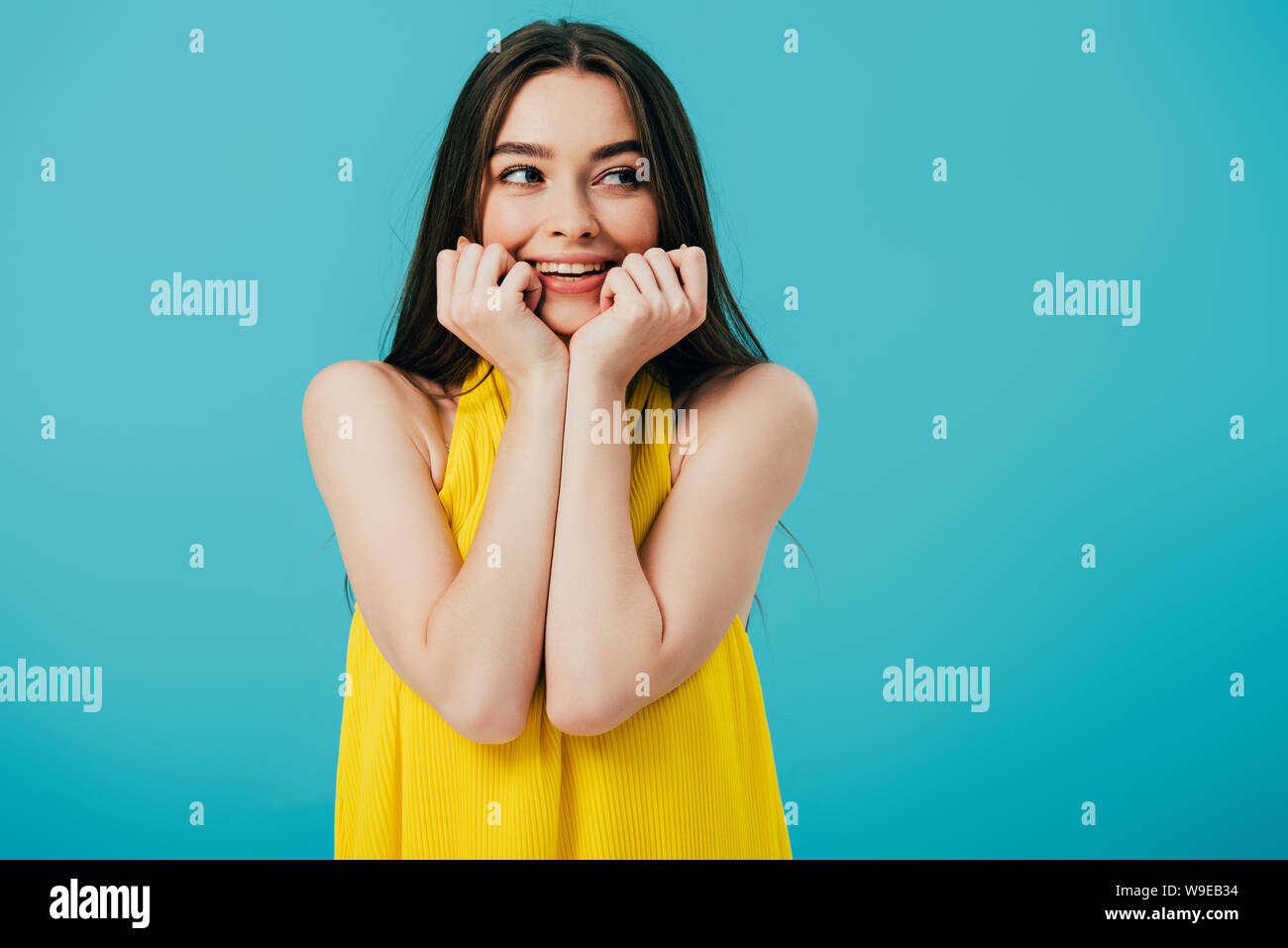 happy beautiful girl in yellow dress with hands near face looking away ...