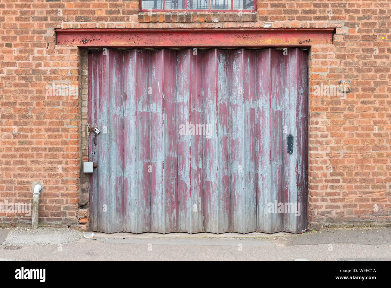 Old worn red roller shutter door on factory with flaking paint Stock Photo
