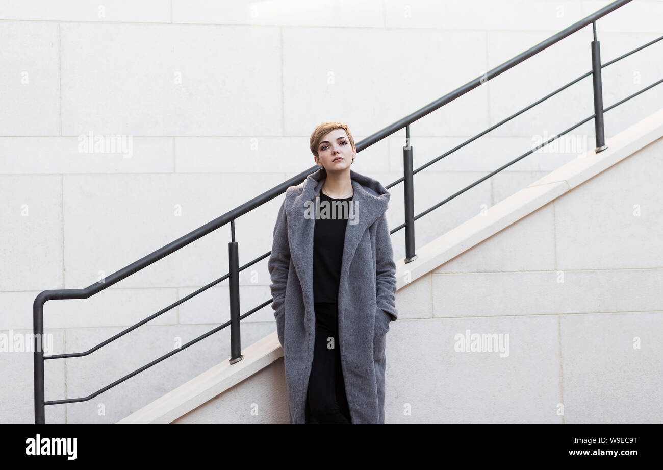 Woman With Short Tousled Hair In Gray Coat On Stairs Background