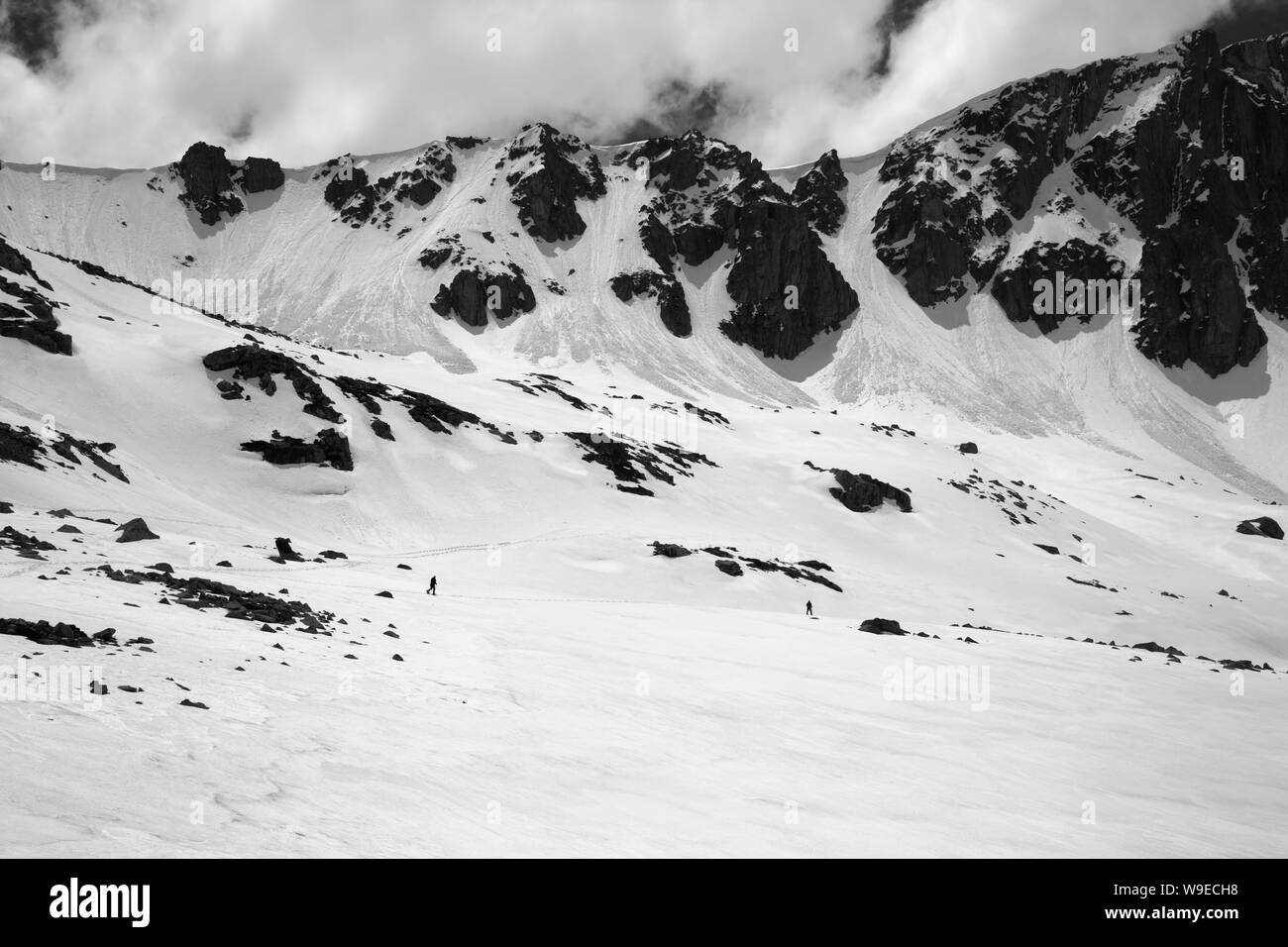 High mountains with snow cornice and avalanche trail, snowy plateau and two small silhouette of hikers at sunny day. Turkey, Kachkar Mountains, highes Stock Photo