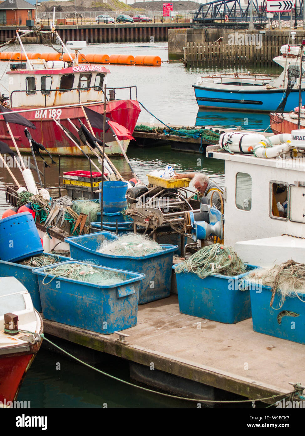 Swansea marina. Fishing boats are tied up at the dock. Fishing equipment and nets are on the dock. A fisherman is working on his boat. Wales, UK. Stock Photo