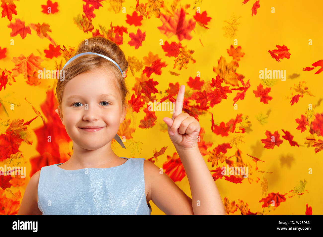 Little girl in a Cinderella princess costume with falling autumn leaves. The child shows the index finger up. Concept for autumn, holiday, halloween, Stock Photo