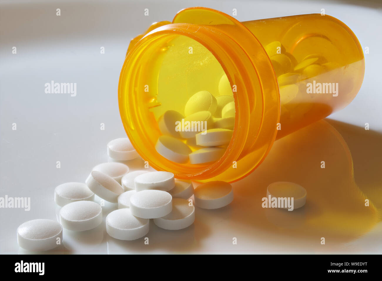 White pills falling out of an unlabeled amber pill bottle lying on its side Stock Photo